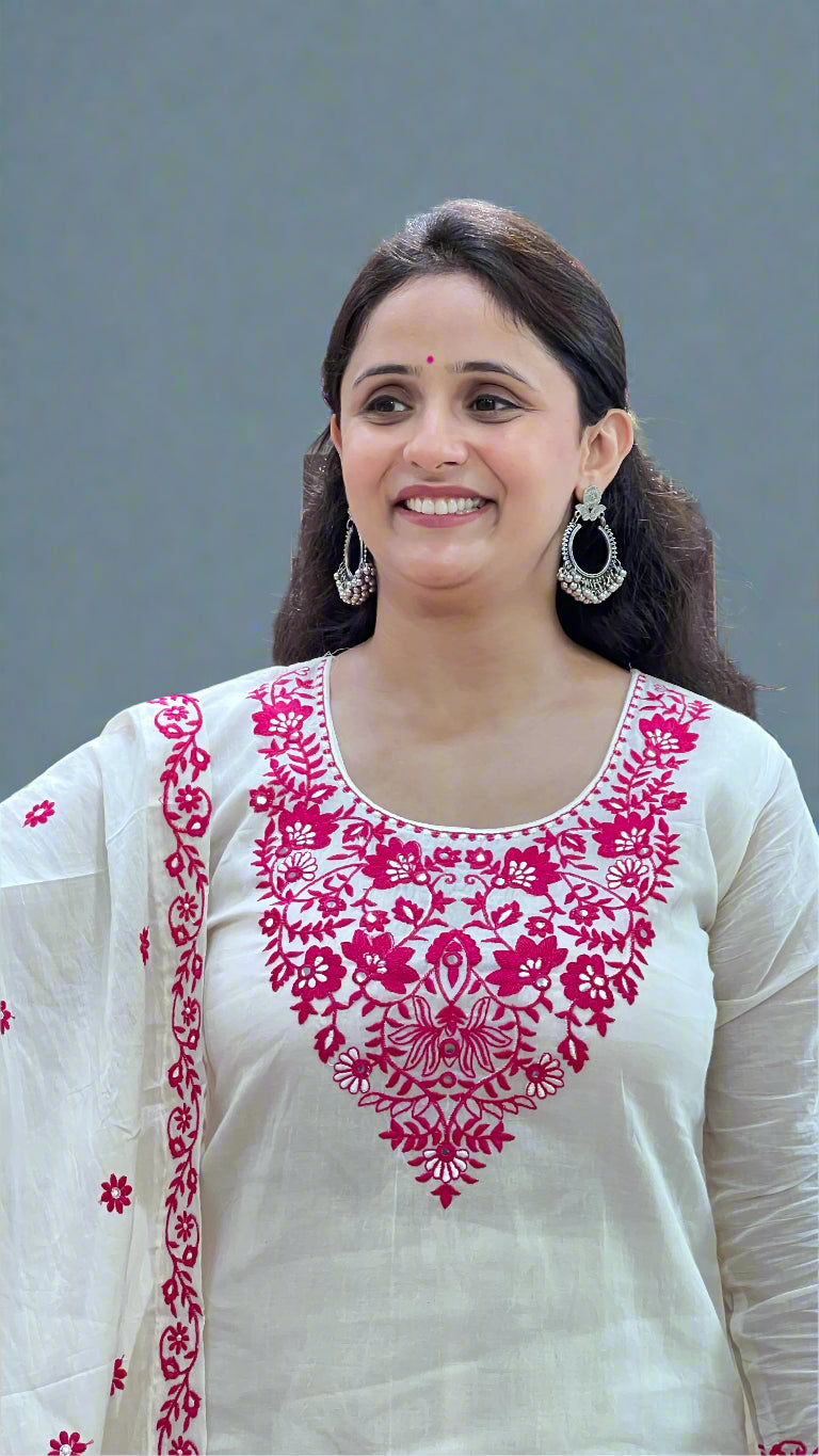 Woman wearing a white outfit with pink embroidery in front of a store sign.