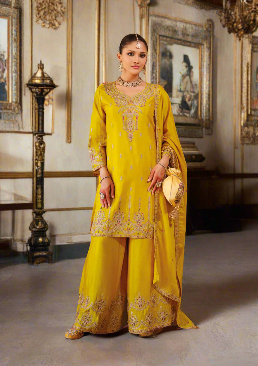 Woman in a yellow embroidered traditional outfit standing in an ornate room.